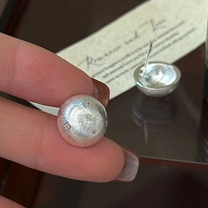 Hand holding brushed S925 silver stud earrings with delicate star pattern engraving
