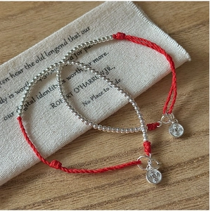 Detailed shot of handmade red cord bracelets with engraved S925 silver charms on linen