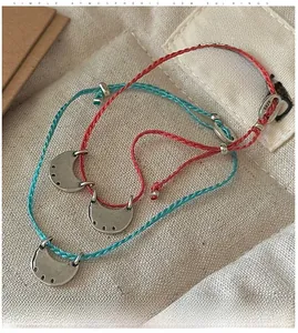 Detailed macro view of S925 sterling silver crescent charms on red and blue woven bracelets