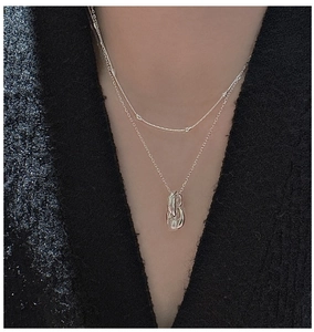 Close-up of layered S925 sterling silver necklaces with twisted geometric pendant on neck