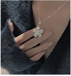 Close-up of a minimalist S925 silver flower pendant necklace on a black knit sweater