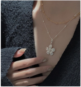 Close-up of S925 silver flower pendant and gold bead chain on a grey sweater