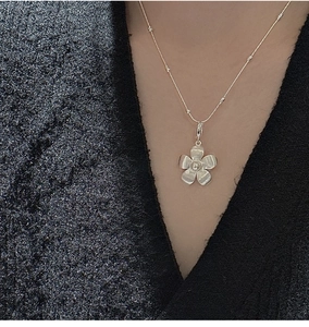 Detailed view of S925 sterling silver flower pendant with brushed texture on black sweater