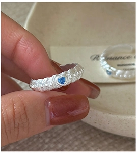 Macro shot of silver ring with blue heart zircon and wavy frosted texture band