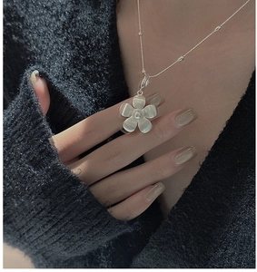 Detail view of S925 sterling silver flower pendant with brushed texture on black sweater
