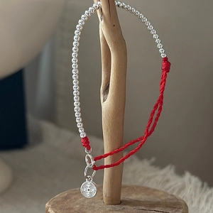 S925 sterling silver red rope bracelet with round peace charm on a wooden stand