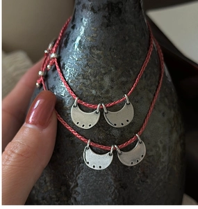 Detail view of red braided rope bracelets with vintage silver half-moon charms on ceramic