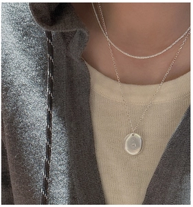 Detail of layered S925 silver tennis chain and coin pendant necklace on a model