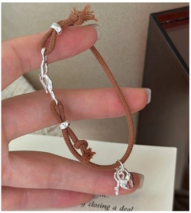 Detail of hand-woven brown rope bracelet with silver heart lock and key charms