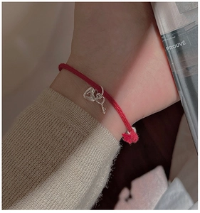 Detail of red braided rope bracelet with silver heart and key charms on a female wrist