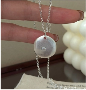 Macro detail of matte silver disc pendant with central cubic zirconia on a dainty chain