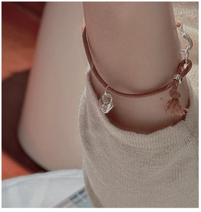 Close-up of woven brown cord bracelet featuring a silver heart lock charm and small tassel