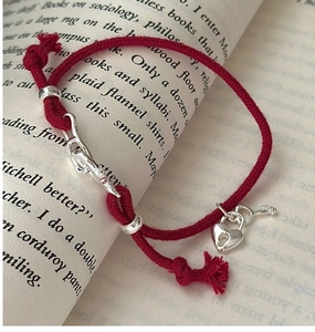 Detail of red braided bracelet with silver heart lock and key charms on vintage book