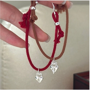 Close-up of woven red and brown couple bracelets with silver heart lock and key charms