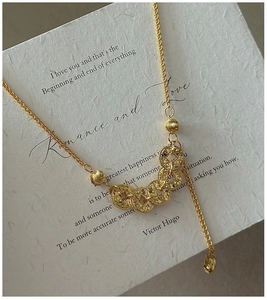 Macro shot of gold necklace with five textured ring pendants on an artistic card