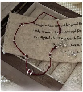 Détail du bracelet en cordon rouge tressé avec perles argentées et breloque zircon