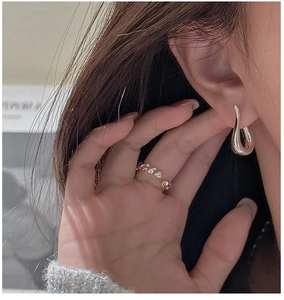 Detail of a silver teardrop earring and gold chain ring worn by a model