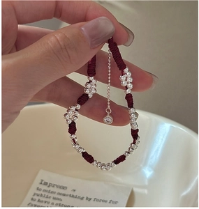 Detail of red woven rope bracelet with silver beads and shimmering diamond pendant
