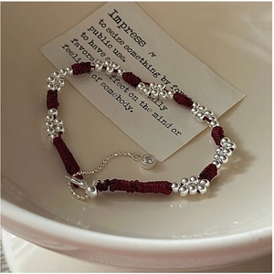 Close-up of woven red rope bracelet with silver floral beads and adjustable zircon pendant