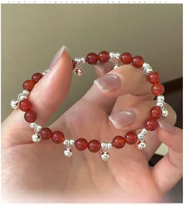 Close-up of red agate beaded bracelet featuring small silver bell charms on the wrist