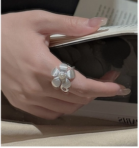 Detailed close-up of a silver floral ring with brushed texture and a white pearl on a finger