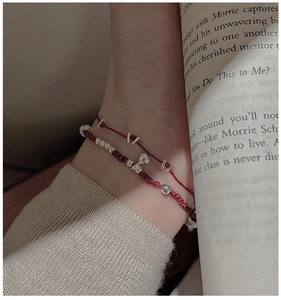 Détail de bracelets tressés rouges en argent S925 au poignet avec un pull en maille doux