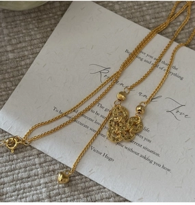Detail of gold coin pendant necklace with textured disks and heart charm on linen background