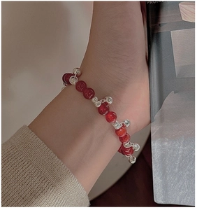 Macro detail of S925 silver bell charms and red agate beaded bracelet on female wrist