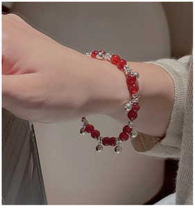 Detail of red agate beaded bracelet with silver bells on a model's wrist wearing knitwear