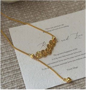 Detail of gold necklace with five textured discs and heart pendant on a soft fabric
