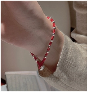 Detailed view of a red woven rope bracelet with silver beads on a wrist with a sweater
