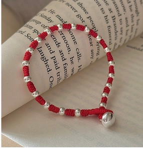 Detailed view of handmade red braided cord bracelet with silver beads on book pages