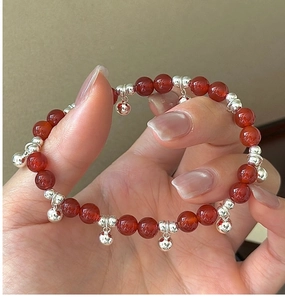 Detail of red agate bead bracelet with silver bells held in hand for a festive look