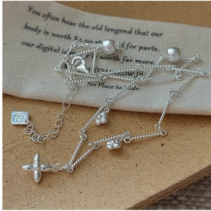 Macro detail of S925 silver floral necklace with pearls and clover charms on texture