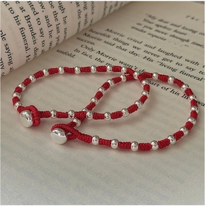 Detail of red woven bracelets with silver beads on a vintage book backdrop