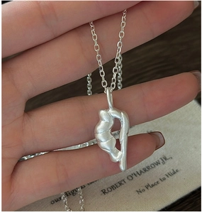 Detail of silver matte abstract pendant with delicate cross chain held in hand