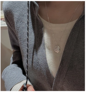 Detail of minimalist S925 silver textured pendant necklace worn on a grey knit cardigan