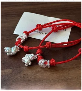 Detail of red string bracelet featuring S925 silver bunny charm and textured rings