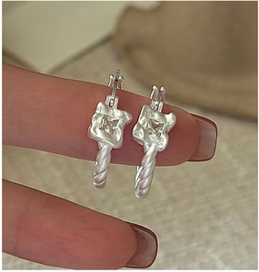 Close-up of S925 silver twist hoop earrings with a central square zircon on a soft fabric