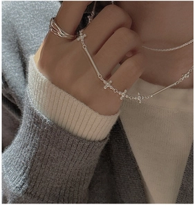 Gros plan sur le collier croix en argent S925 et l'ensemble de bagues minimalistes
