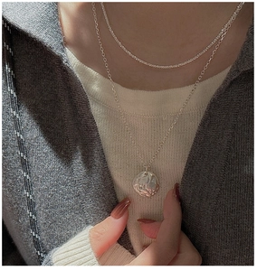 Detail view of double-layered S925 silver necklace with textured round pendant on neck