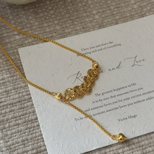 Elegant gold woven necklace featuring micro-coin charms and a polished heart pendant