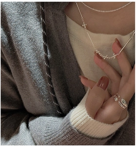 Gros plan sur une bague large en argent et un collier de perles sur un pull en maille