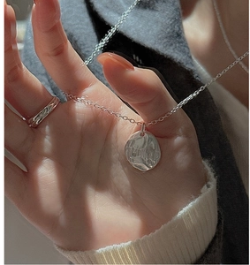 Close-up of S925 sterling silver hammered pendant necklace and textured ring on a model