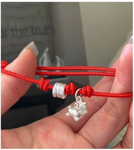 Close-up of red braided rope bracelet with silver zodiac ox and cylinder charm