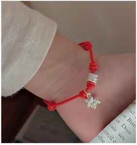 Detail of S925 sterling silver pig charm and red braided bracelet on a wrist
