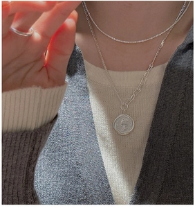 Close-up of layered silver coin pendant necklace and sparkling crystal tennis chain