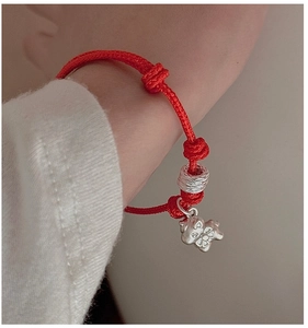 Detail of red handmade woven rope bracelet featuring a silver pig charm and matte bead