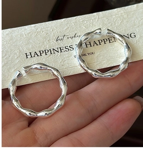 Detailed view of silver wave texture hoop earrings held by hand for quality display
