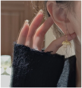 Close-up of a gold umbrella-shaped earring in matte finish worn by a model
